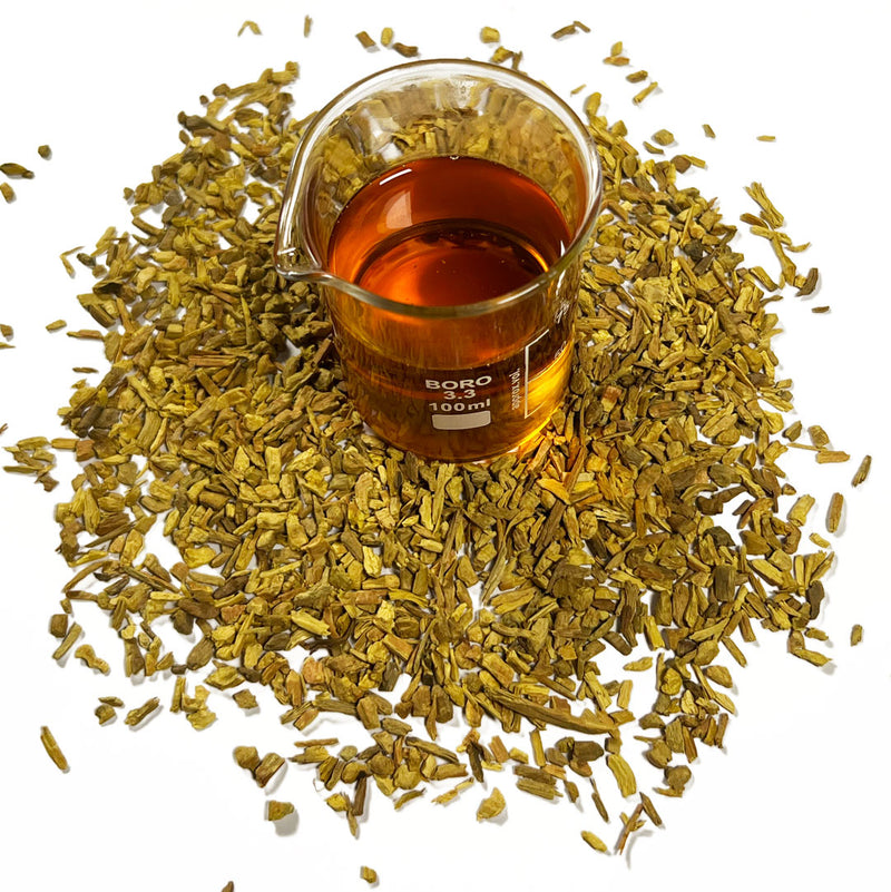 Barberry bark chips (Berberis vulgaris) surrounds a beaker with Barberry Bark Cellular Extract, golden orange in colour