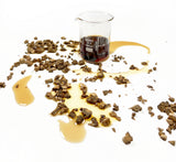 Burdock root scattered around Burdock Cellular Extract sitting in a beaker, yellow to brown in colour