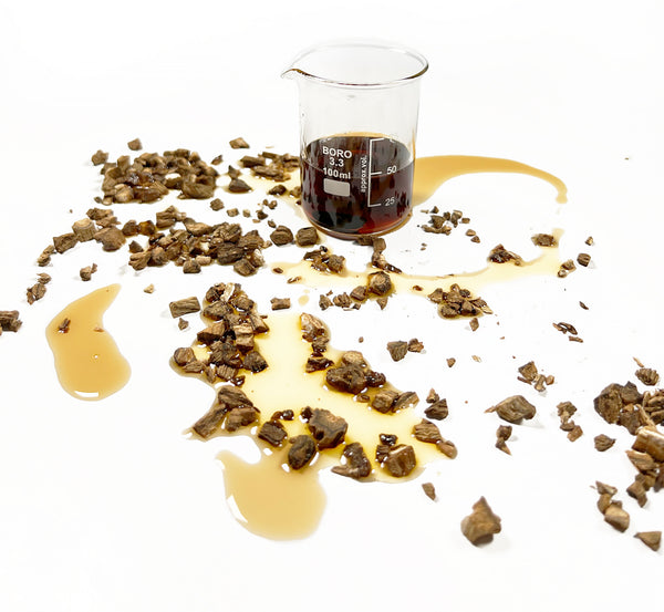 Burdock root scattered around Burdock Cellular Extract sitting in a beaker, yellow to brown in colour