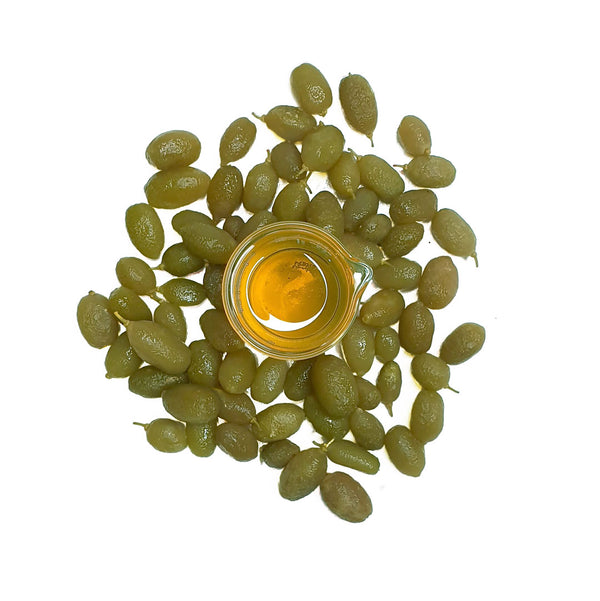 Cellular Extract of Desert Lime light yellow in colour in a beaker with fresh deserts limes surrounded, scientifically known as Citrus glauca