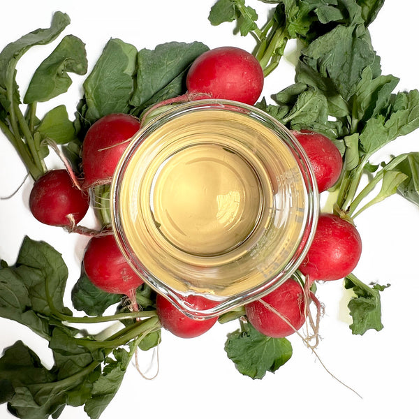A beaker of the Native Extracts Radish Cellular Extract sits on a bench, surrounded by radish leaves and roots.