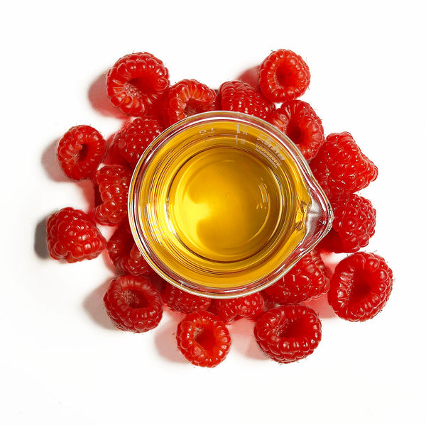 Numerous raspberries (Rubus idaeus), surround a beaker of the Native Extracts Raspberry Cellular Extract.