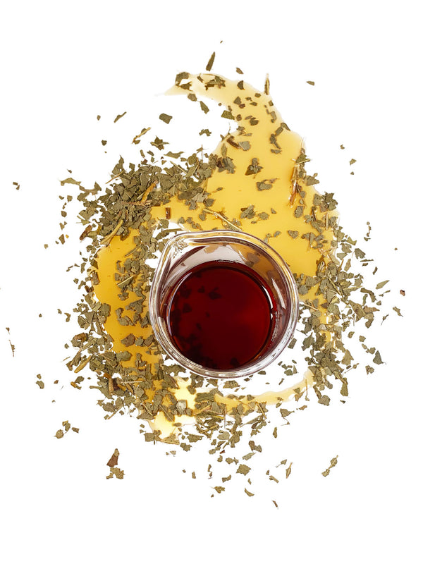 Dried Tasmanian Blue Gum leaves (Eucalyptus globulus), surround a beaker of Native Extracts Tasmanian Blue Gum Cellular Extract, which is dark red in colour.